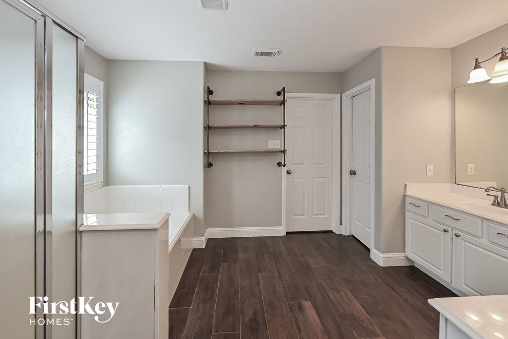 a bathroom with white cabinets and a white sink and a shower and a wooden floor