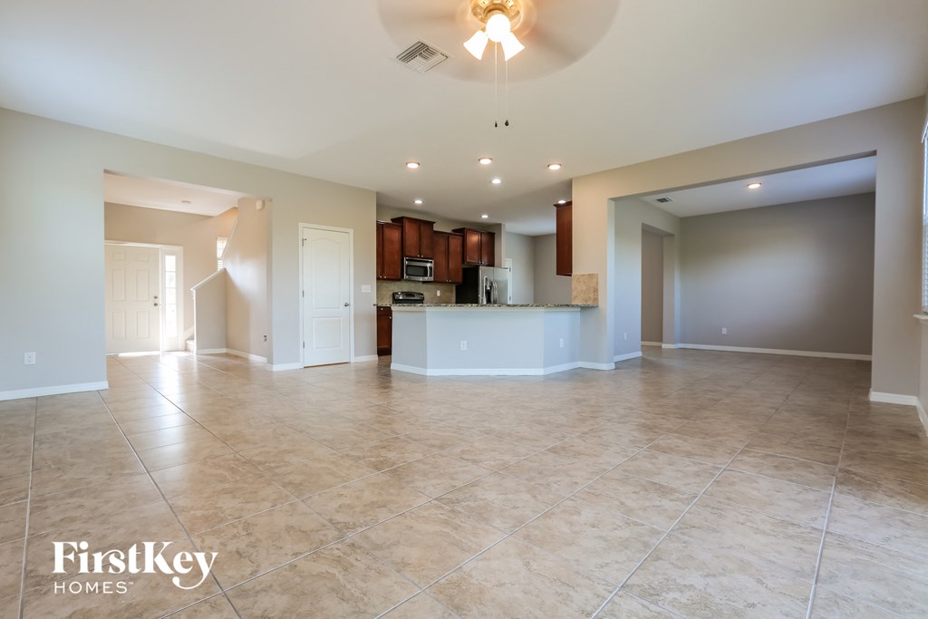 an empty living room with a kitchen and a ceiling fan