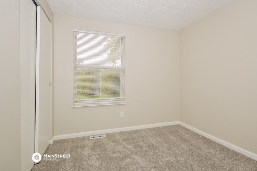 the living room of a studio apartment with carpet and a window