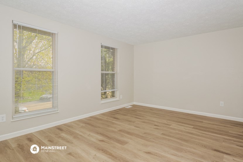 a spacious living room with wood flooring and two windows