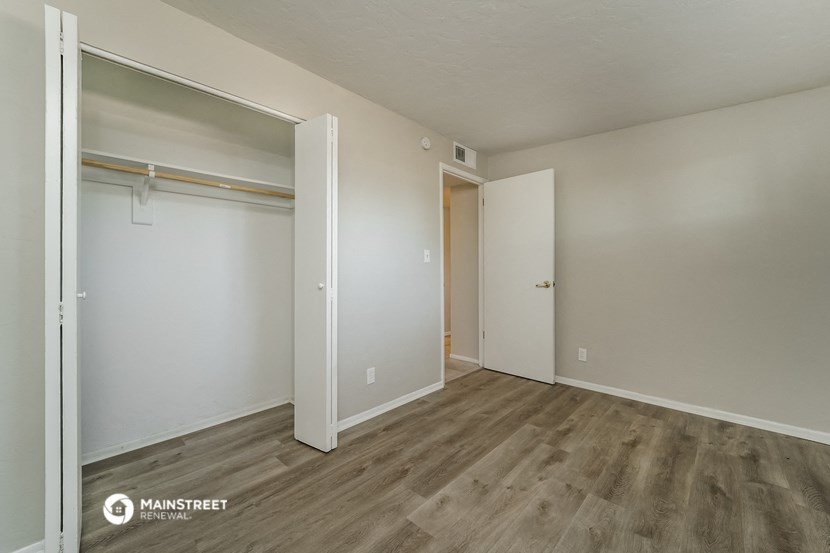 a bedroom with white walls and wood flooring and a closet