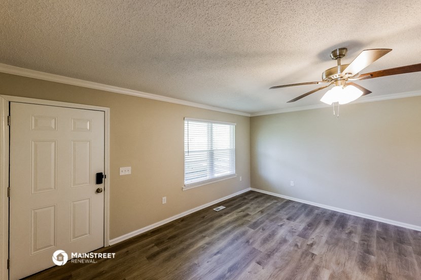 the spacious living room with a ceiling fan and a white door