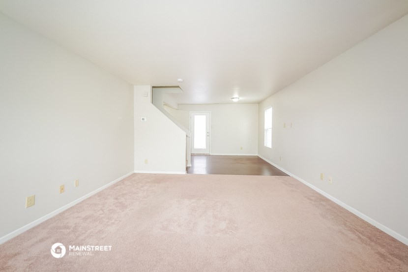 the living room and dining room of a home with white walls and carpet
