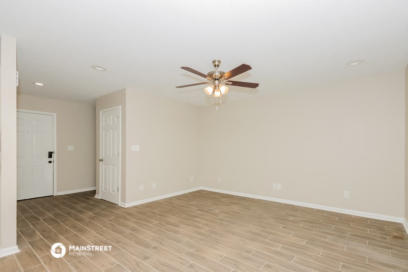 the spacious living room with wood flooring and a ceiling fan