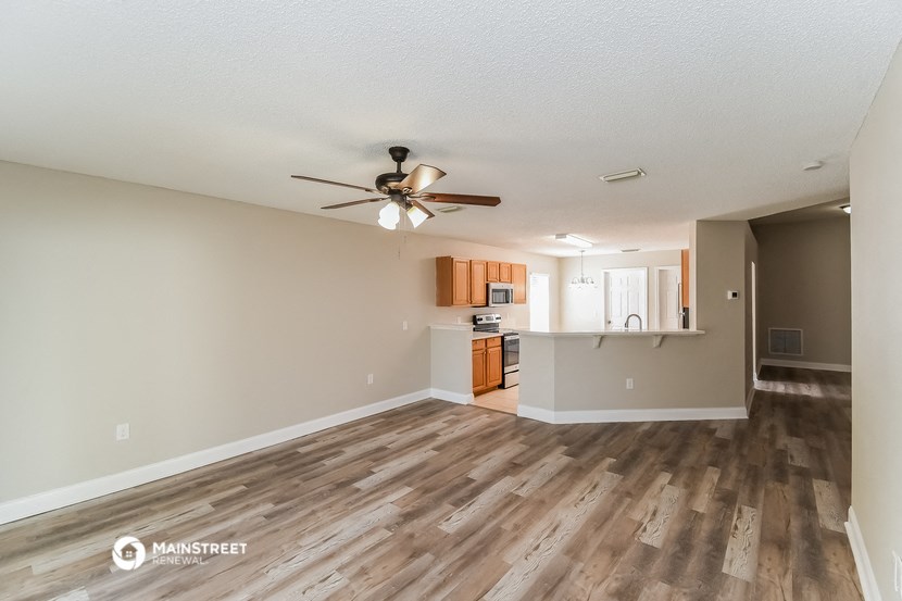 an empty living room with a ceiling fan and a kitchen