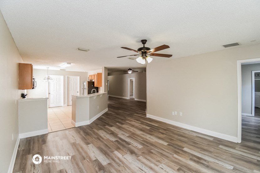 an empty living room with a ceiling fan and a kitchen