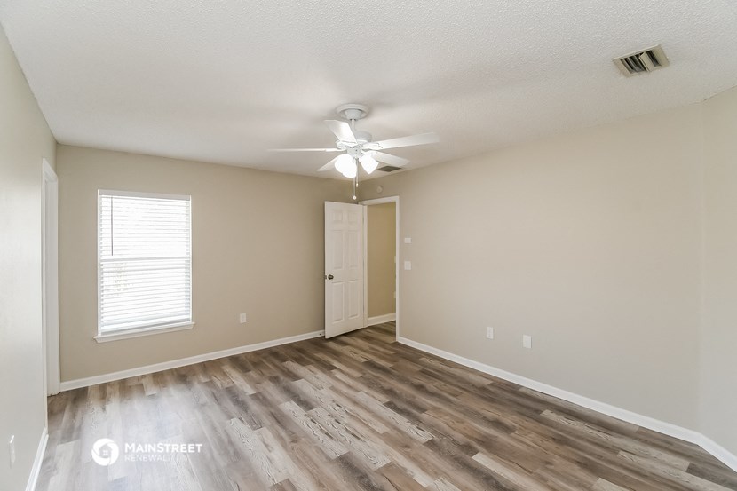 the spacious living room with hardwood flooring and a ceiling fan