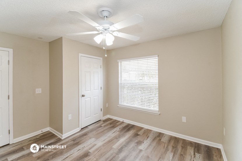 the spacious living room with a large window and a ceiling fan