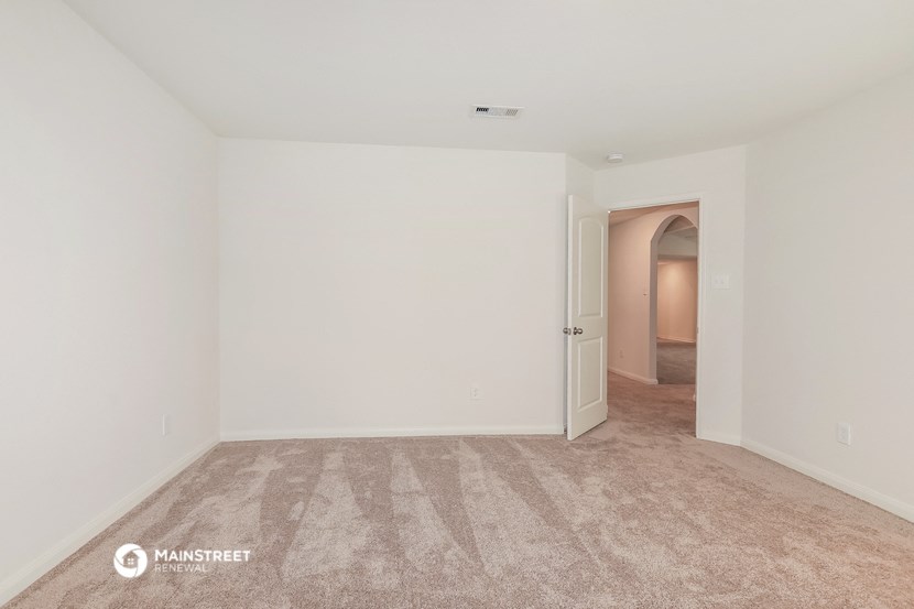 a bedroom with white walls and carpet and a door to a hallway