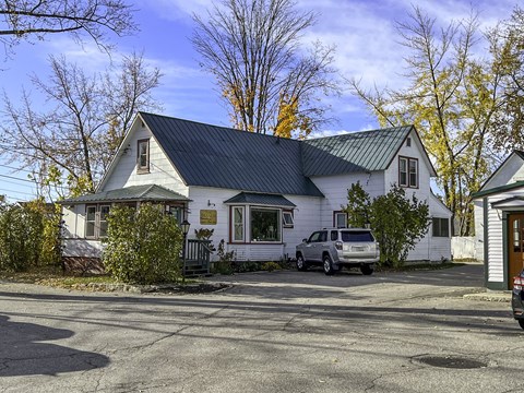 A white house with a black roof and a silver car parked in front.