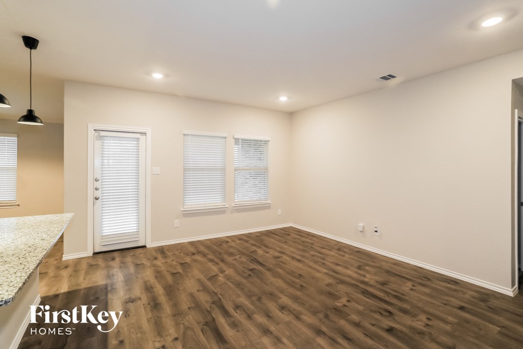 A spacious room with wooden flooring and white walls, featuring a kitchen counter and a door.