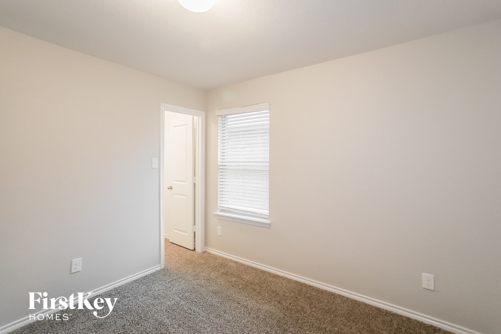 A room with a carpeted floor, a door, and a window with blinds.