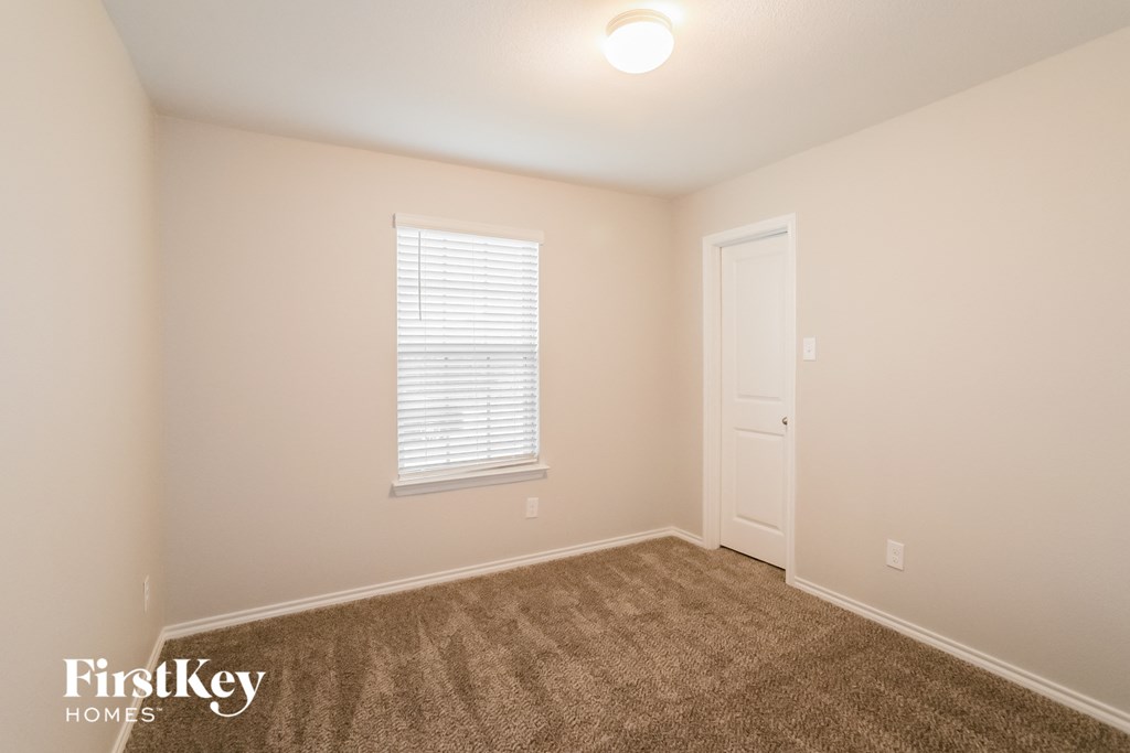 A room with a carpeted floor, a window with blinds, and a door.