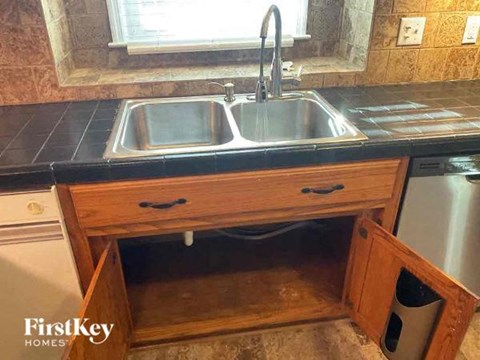 A kitchen sink under a window with a wooden drawer underneath.