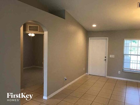 an empty living room with a door to a hallway and a tiled floor