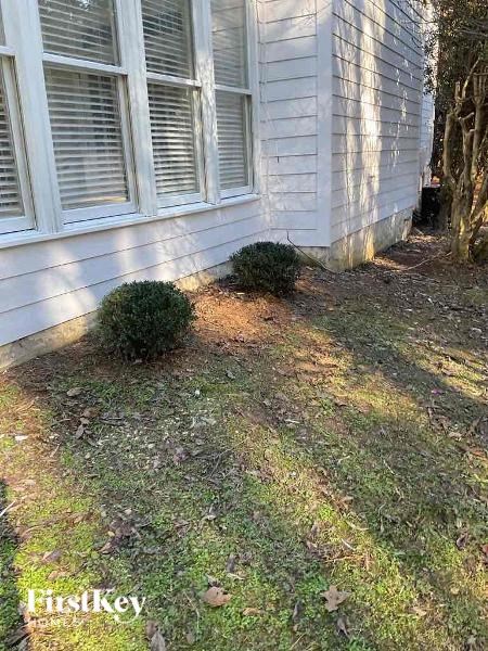 the side of a white house with grass and bushes