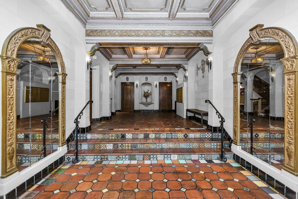 A hallway with a tiled floor and ornate gold framed mirrors on the walls.
