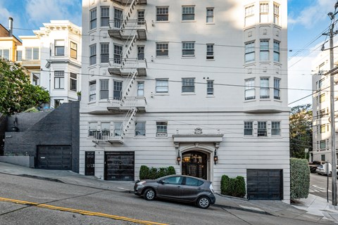 A white building with a grey car parked in front.