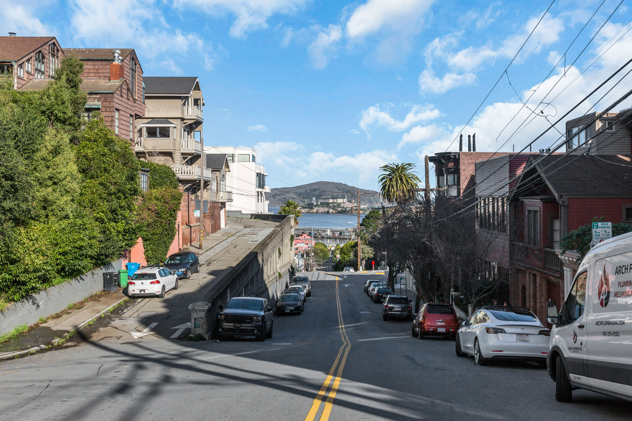 A street view with cars parked on the side and a white van parked on the side of the road.