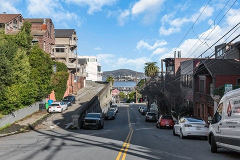 A street view with cars parked on the side and a white van parked on the side of the road.