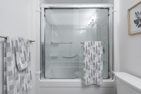 a white bathroom with a glass shower door and two towels