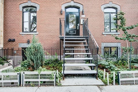 A red brick house with a black door and a metal railing.
