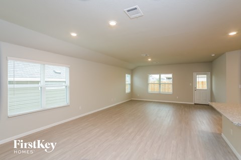 A spacious empty room with wooden flooring and a window with blinds.