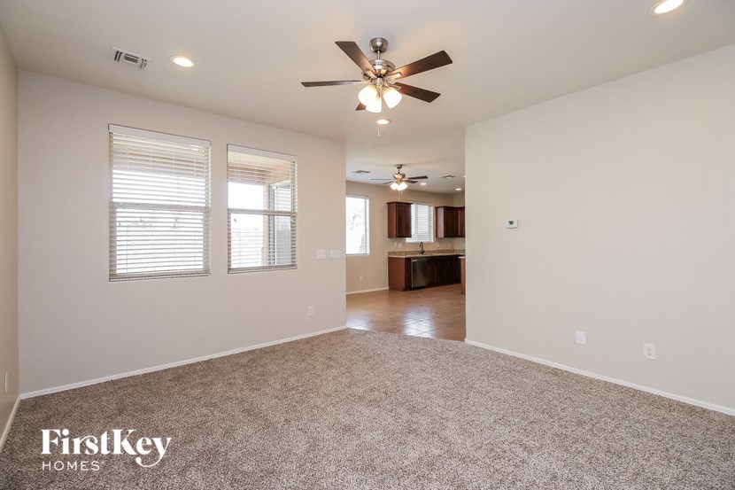 an empty living room with a ceiling fan and a kitchen
