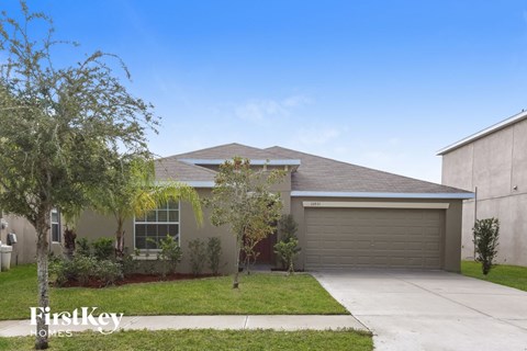 a beige house with a driveway and trees