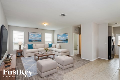 A spacious living room with a white sofa set and a painting on the wall.