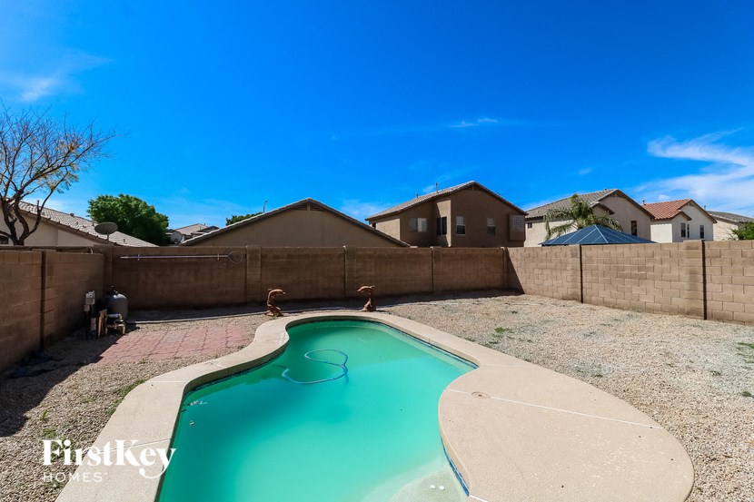 A swimming pool in a backyard with a concrete floor and a concrete wall.