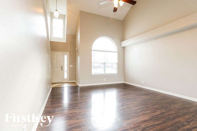A spacious room with wooden floors and a large arched window.