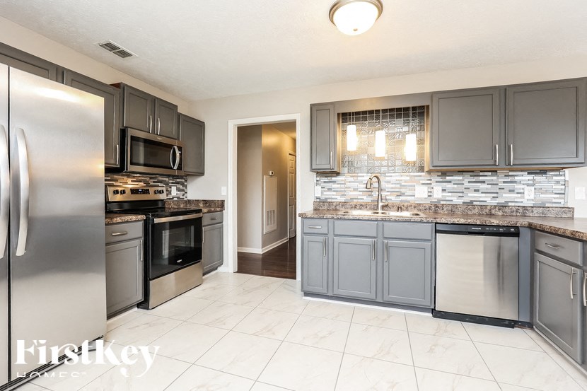 A kitchen with a refrigerator, microwave, oven, and sink.