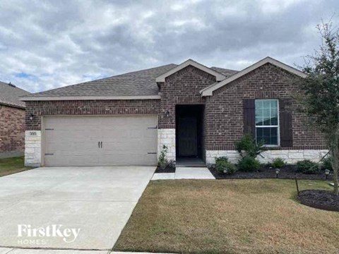 A brick house with a garage door and a tree in front.