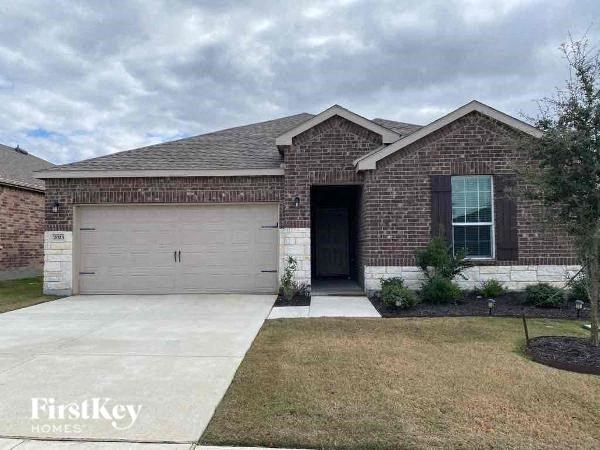 A brick house with a garage door and a tree in front.