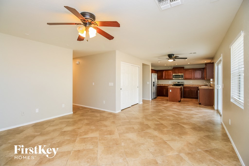 an empty living room with a ceiling fan and a kitchen