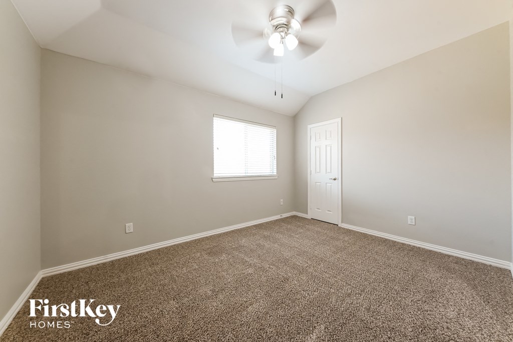 A room with a carpeted floor, a ceiling fan, and a door.