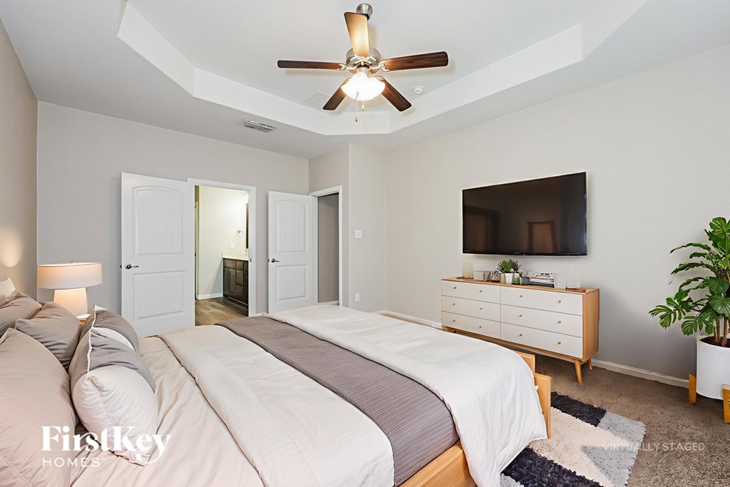 A bedroom with a large bed, a ceiling fan, and a TV mounted on the wall.