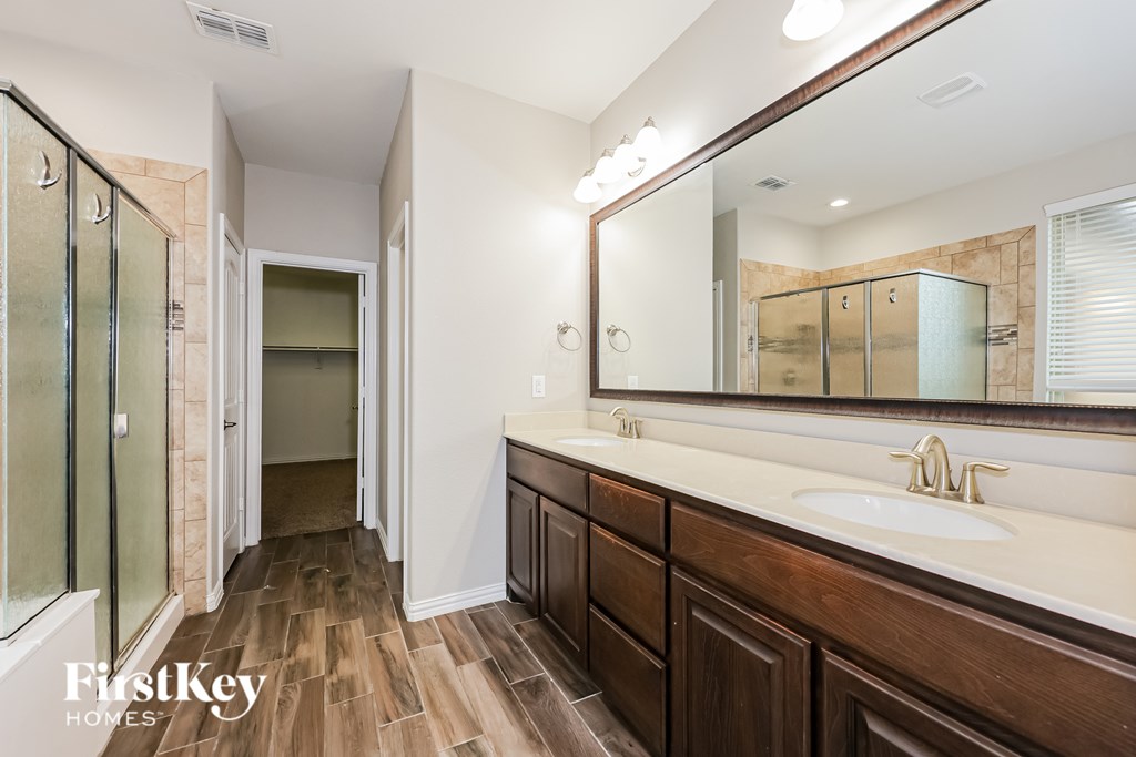 A bathroom with a wooden floor and a large mirror above the sink.