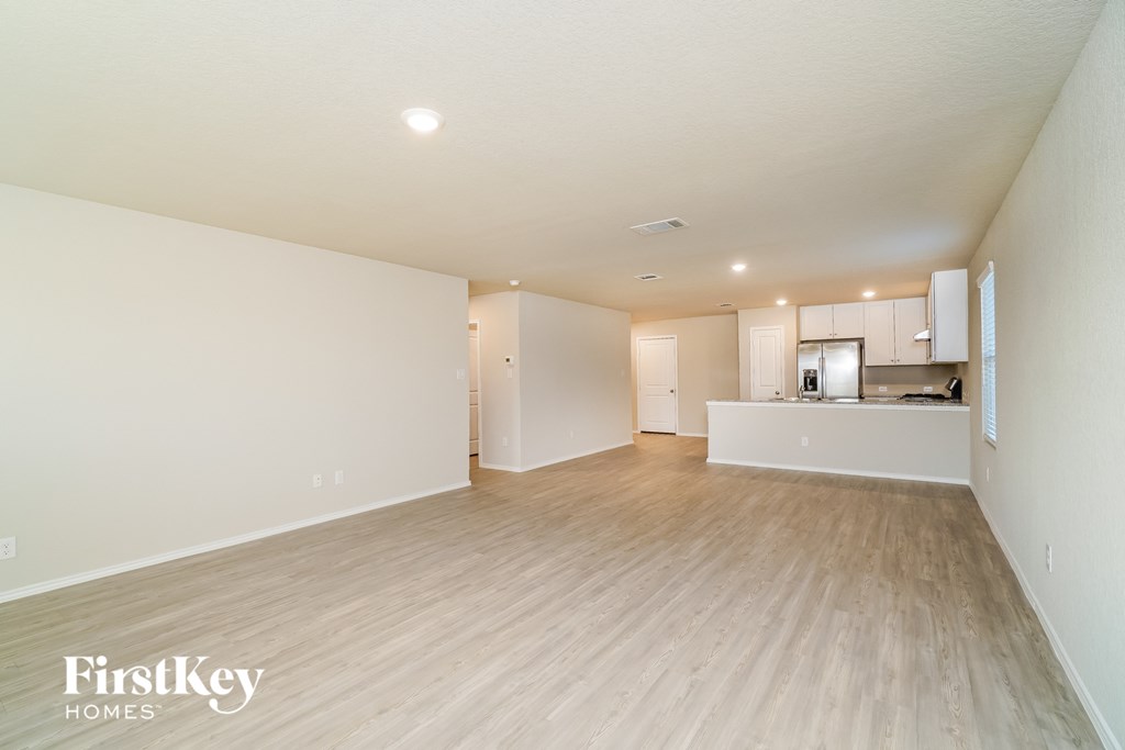 a spacious living room and kitchen with white walls and wood flooring