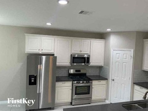 A kitchen with a stainless steel refrigerator and black countertops.