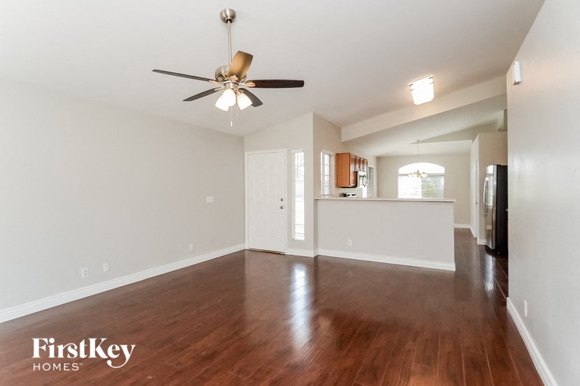 an empty living room with a ceiling fan and a kitchen