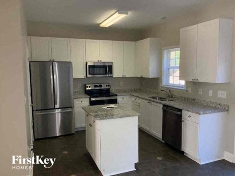 A kitchen with a refrigerator, microwave, oven, sink, and cabinets.