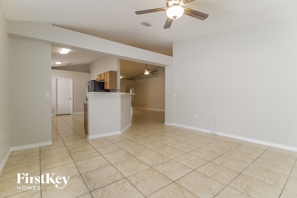 a spacious living room with tile flooring and a kitchen with a ceiling fan