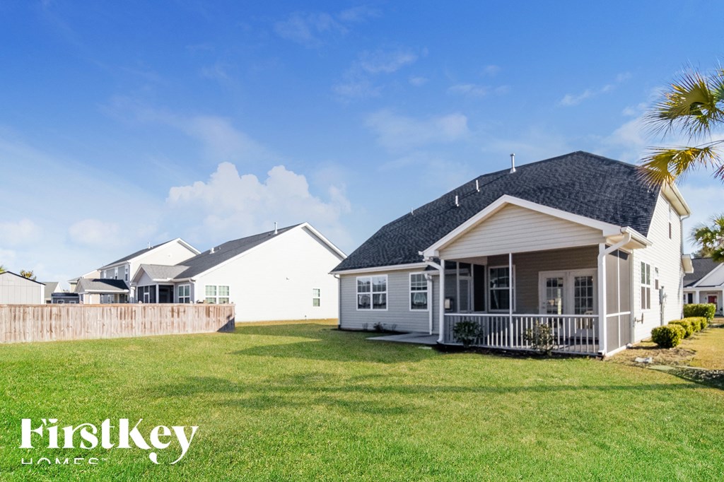 A house with a white exterior and a black roof is surrounded by a wooden fence and has a well-manicured lawn.
