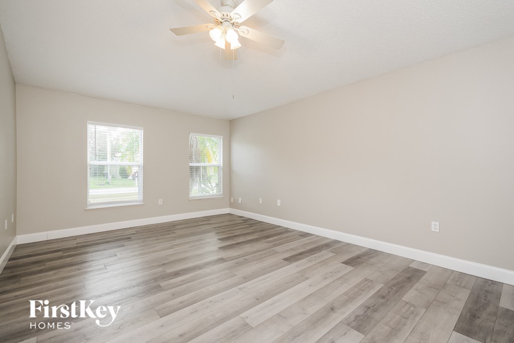 the spacious living room with hardwood flooring and a ceiling fan