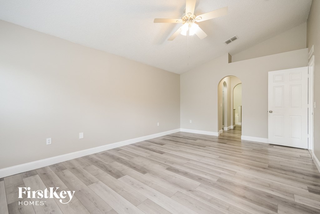 the spacious living room with hardwood flooring and a ceiling fan