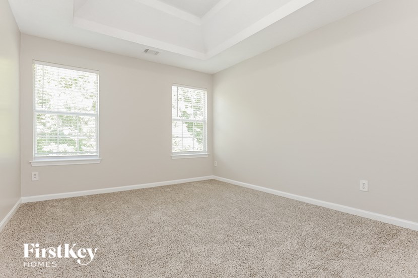 an empty bedroom with two windows and carpeting