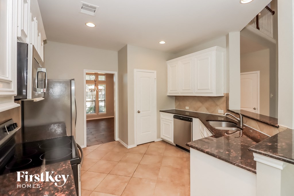 a kitchen with black countertops and white cabinets and a door to a hallway