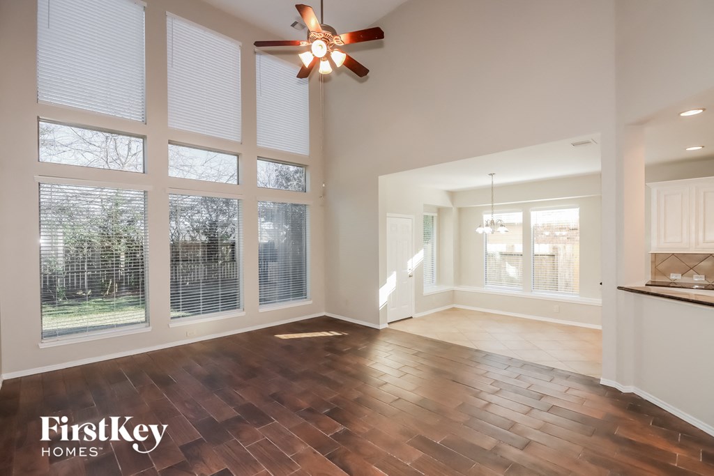 an empty living room with large windows and a ceiling fan